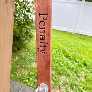 Puede incluir: Un soporte de madera para vasos de chupito con la palabra "Penalty" grabada en &eacute;l. Un vaso de chupito est&aacute; unido al soporte.