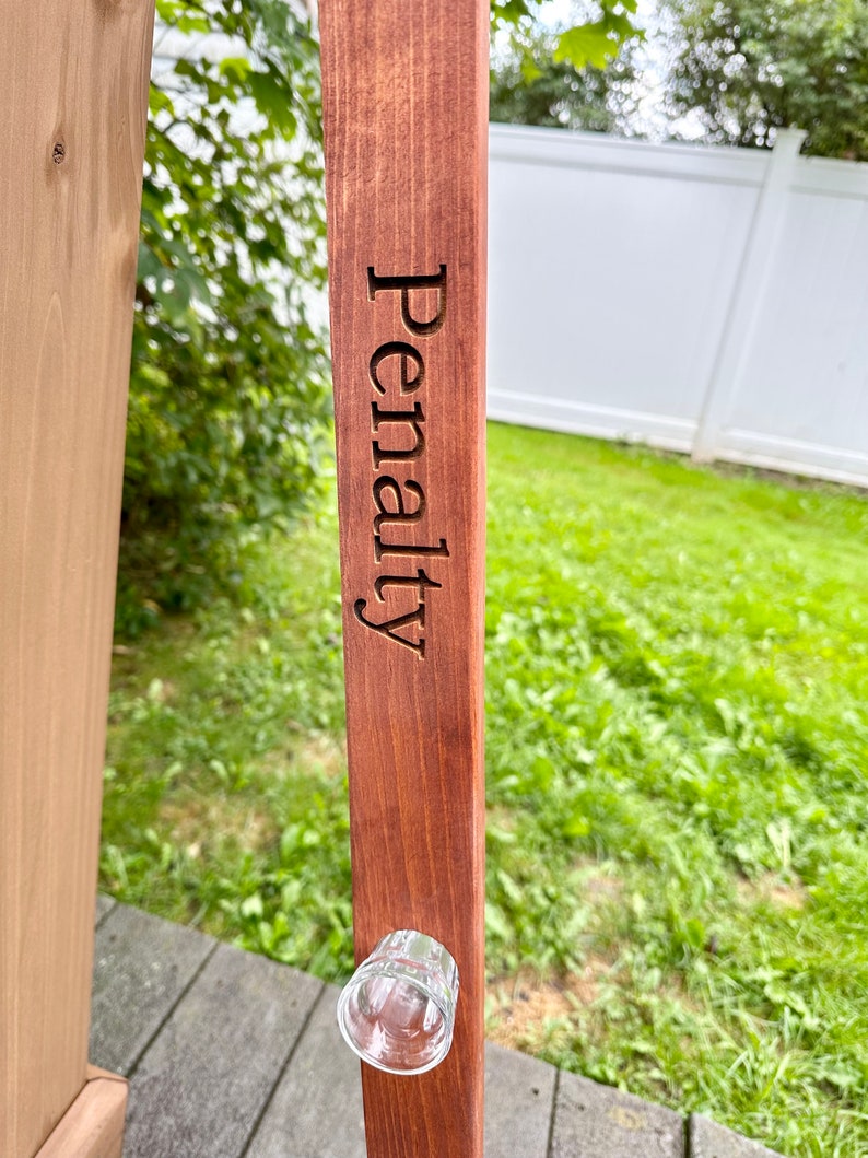 Puede incluir: Un soporte de madera para vasos de chupito con la palabra "Penalty" grabada en &eacute;l. Un vaso de chupito est&aacute; unido al soporte.