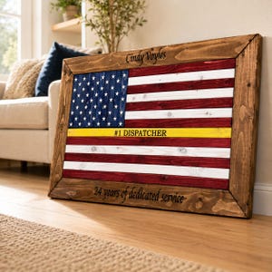 May include: A rectangular wooden wall art piece featuring a painted American flag with a yellow horizontal stripe, inscribed with the text Cindy Voyles, #1 DISPATCHER, and 24 years of dedicated service, framed in dark stained wood.