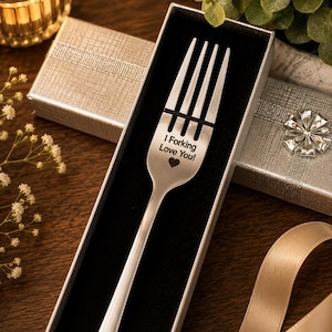 May include: A silver-toned metal fork with a matte finish, presented in a rectangular gift box with a black velvet interior. The fork is engraved with the text "I Forking Love You!" followed by a small heart symbol centered on the handle.