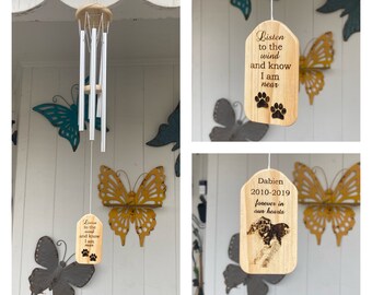 May include: A wooden wind chime with a paw print design and the text "Listen to the wind and know I am near". The chime is hanging from a hook on a white wall. There are also two other wooden tags with paw print designs and text that say "Dabien 2010-2019 forever in our hearts" and "Listen to the wind and know I am near".