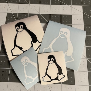 May include: Three penguin stickers, one black and white, one white, and one black. The stickers are on a gray surface.
