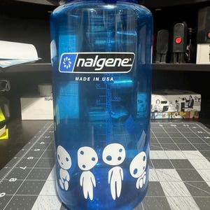 May include: A blue Nalgene water bottle with a white sticker of four white characters with black eyes. The sticker says "nalgene" and "MADE IN USA".