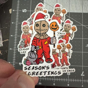 May include: A set of Christmas-themed stickers featuring a character in a red and white Santa suit holding a candy cane with a bitten pumpkin on top. The text "Season's Greetings" is printed on the bottom of the sticker.