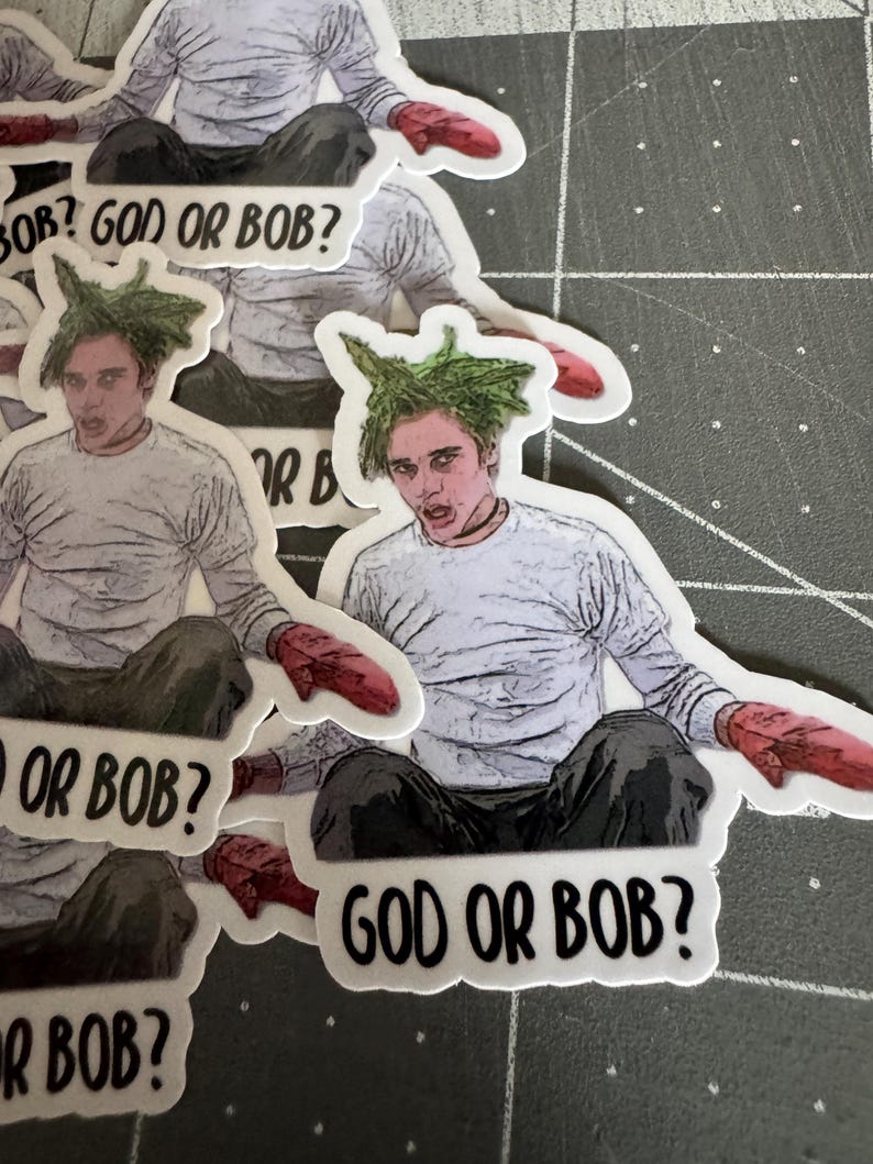 May include: A set of stickers featuring a cartoon character with green hair and the text "God or Bob?" The character is wearing a white shirt and red mittens.
