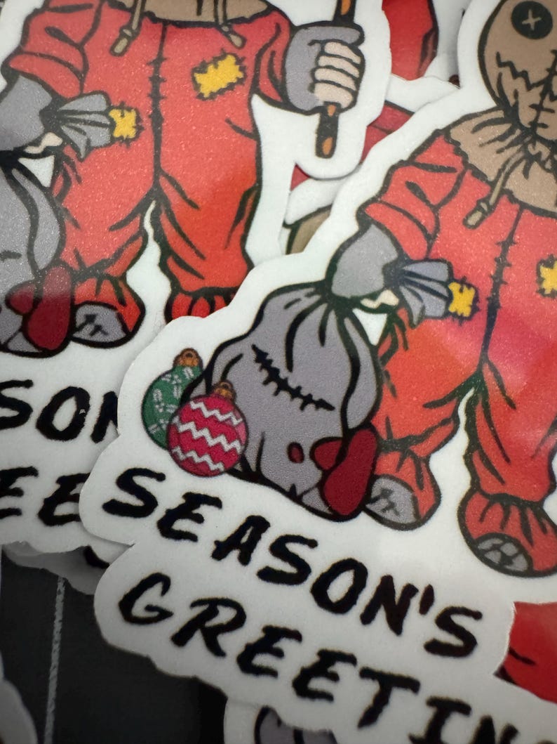 May include: Two red and white Christmas stickers featuring a character in a red jumpsuit holding a sack and a stick. The stickers have the text "Season's Greetings" on them.