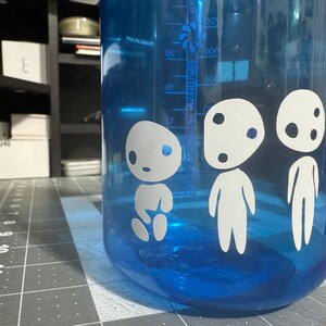 May include: Blue water bottle with white cartoon characters on the side. The characters have large eyes and round bodies. The bottle has a measurement scale on the side.