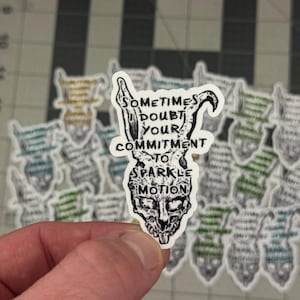 May include: A white sticker with a skull design and the text "Sometimes doubt your commitment to sparkle motion." The skull has rabbit ears and is surrounded by other stickers with similar designs.