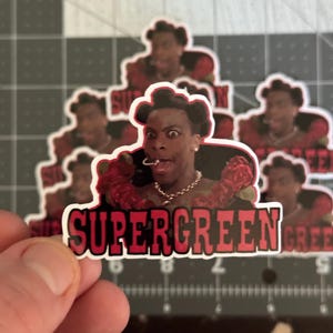 May include: A sticker featuring a close-up of a man with a surprised expression, wearing a red and black outfit with roses. The text "SUPERGREEN" is printed in red and black letters on a white background.