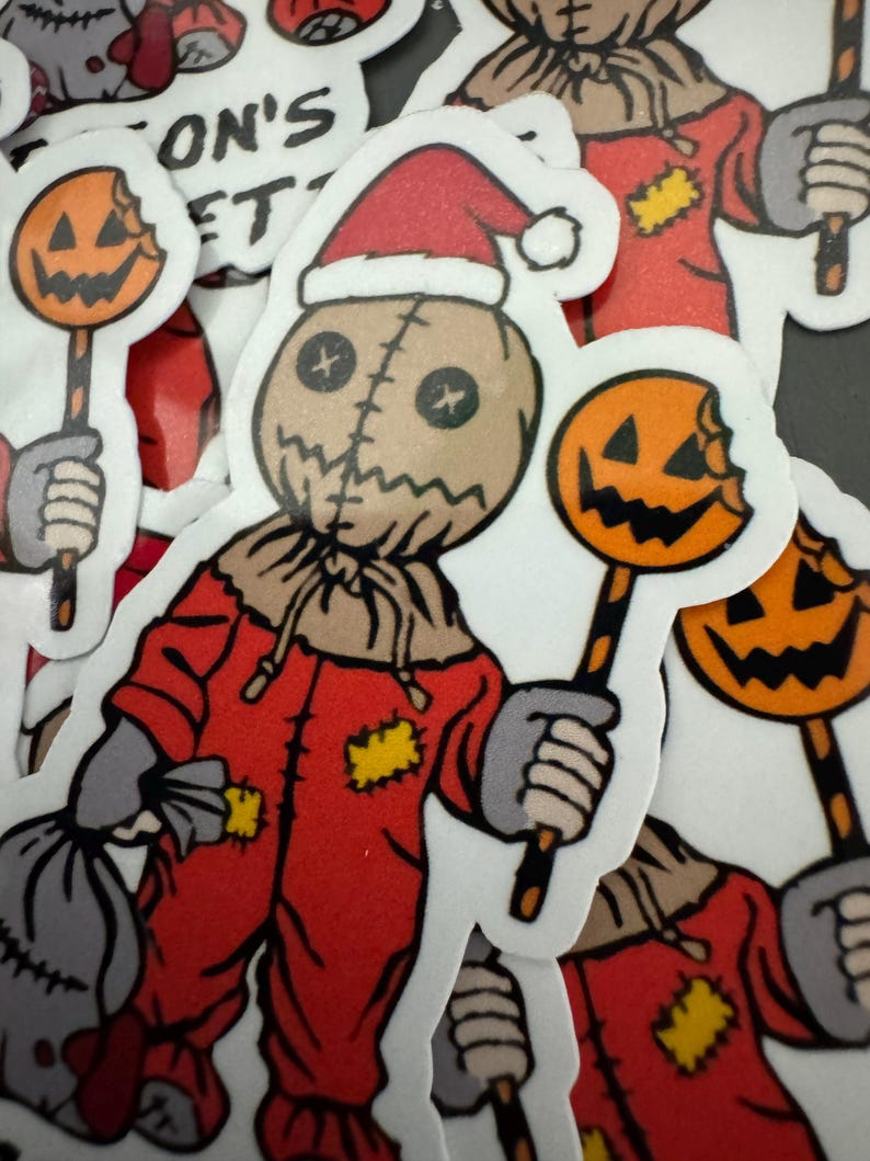 May include: A red and brown Halloween sticker of a character wearing a Santa hat and holding a candy cane with a bitten pumpkin on the end. The character has a stitched face and is wearing a red jumpsuit with yellow patches.