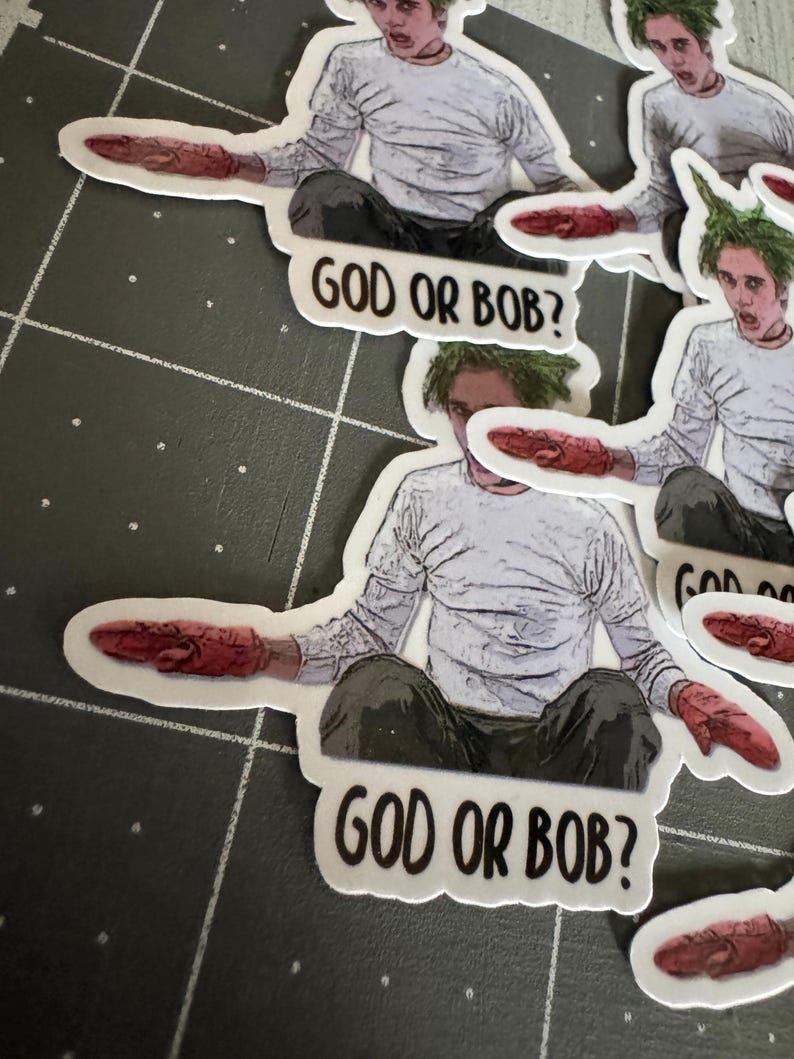 May include: Four stickers featuring a cartoon character with green hair and a white shirt. The character is holding a red object in their hand. The stickers have the text "God or Bob?" printed on them.