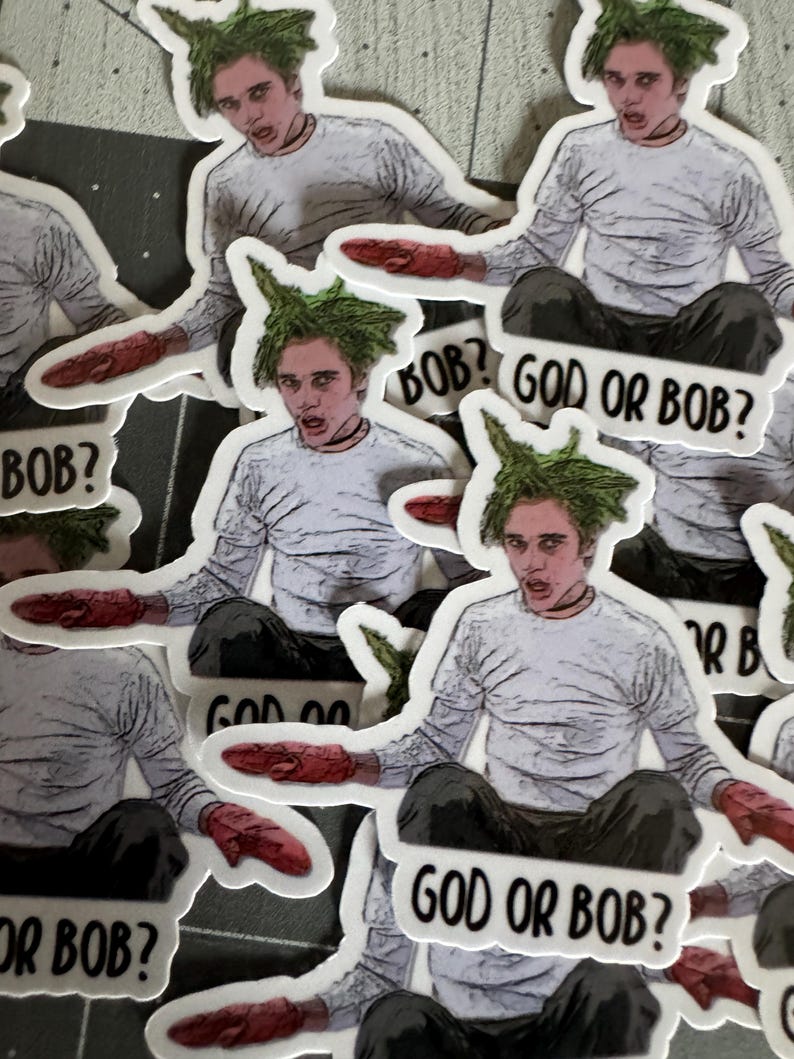 May include: A set of stickers featuring a cartoon character with green hair and a white shirt. The character is holding a red object in their hand. The stickers have the text "God or Bob?" printed on them.