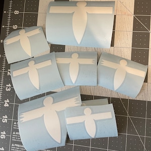 May include: A set of eight white vinyl decals in the shape of a person with outstretched arms. The decals are on a light blue background.