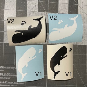 May include: Four vinyl stickers featuring whale designs. Two stickers have a black whale with a paw print, and the other two have a white whale with a paw print. The stickers are labeled V1 and V2.