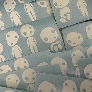 May include: A close-up of a pile of blue vinyl stickers featuring white outlines of a character with two eyes and a mouth. The character is in various poses and sizes.