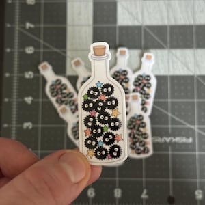 May include: A sticker of a glass bottle filled with black and white fuzzy creatures with colorful stars. The bottle has a cork stopper.