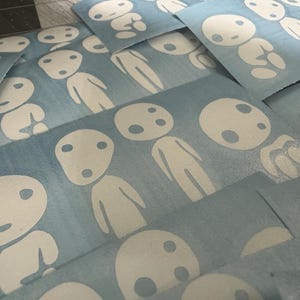 May include: A stack of blue vinyl stickers with white outlines of a character with a round head and two eyes. The character is repeated multiple times on each sticker.