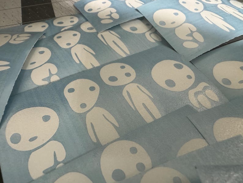May include: A stack of blue vinyl stickers with white outlines of a character with a round head and two eyes. The character is repeated multiple times on each sticker.