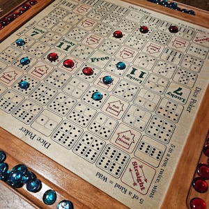 May include: A wooden game board with a beige playing surface and a brown wooden frame. The board has a grid of squares with black dots and dice symbols. There are red and blue glass game pieces on the board. The board has the text "Dice Poker" and "Lucky 7" printed on it.
