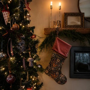 May include: A decorated Christmas tree with ornaments and lights, next to a fireplace. A patterned Christmas stocking hangs from the mantel. Two lit candles and a framed picture are also on the mantel.