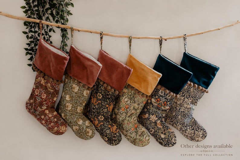 May include: Six Christmas stockings hanging from a wooden branch. The stockings have floral patterns in various colors, with velvet cuffs in shades of red, yellow, and teal. The text "Other designs available" is visible.