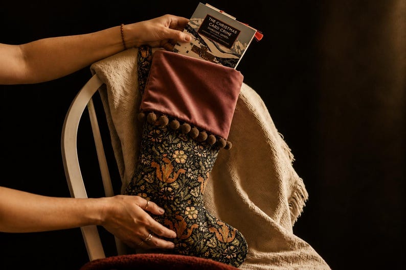 May include: A Christmas stocking with a floral and squirrel pattern, topped with a mauve velvet cuff and brown pom-poms. The stocking is filled with a book titled "The Christmas Card Crime". The stocking is resting on a chair.