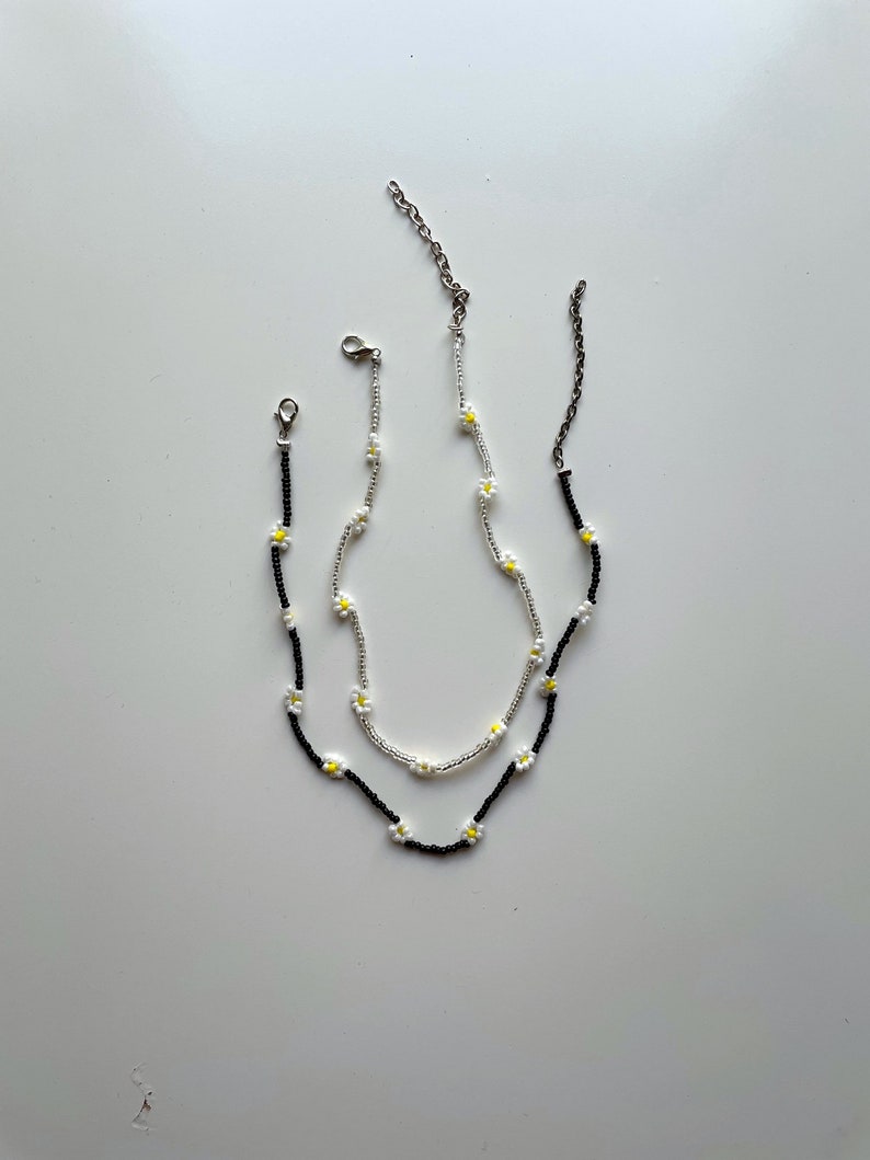 May include: Two delicate necklaces with daisy flower charms. One necklace is black and the other is silver.