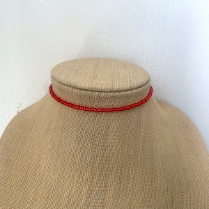 May include: A red beaded choker necklace on a fabric mannequin.