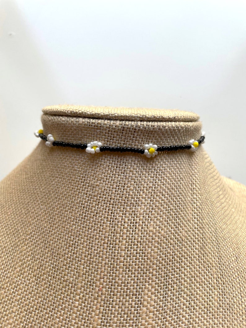 May include: A black beaded choker necklace with small white daisy flowers with yellow centers.