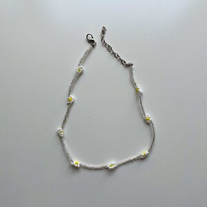 May include: A silver chain necklace with small white daisy flowers with yellow centers.