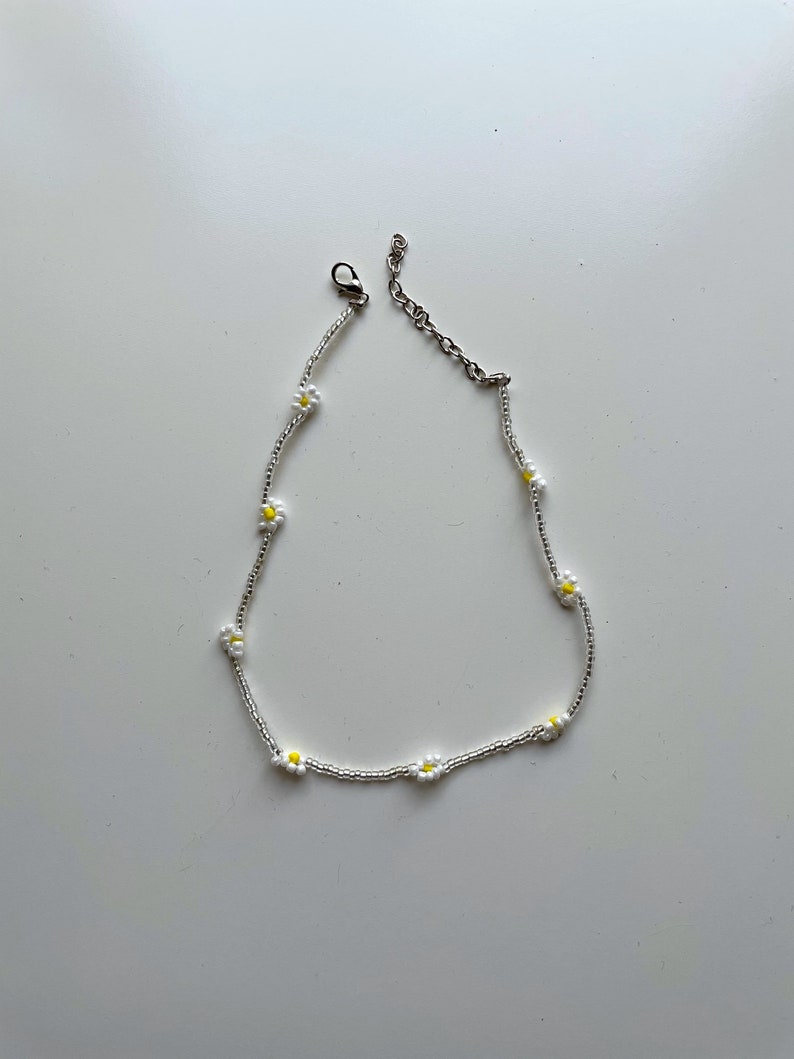 May include: A silver chain necklace with small white daisy flowers with yellow centers.