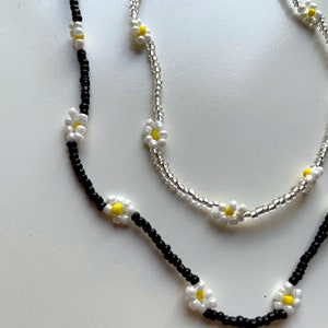 May include: Two necklaces with white daisy flower beads. One necklace has black beads and the other has clear beads.