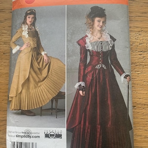 Może przedstawiać: Koperta z wykrojem do szycia Simplicity z dwiema kobietami w historycznych sukniach. Koperta jest pomarańczowo-biała z numerem 2172. Sukienki są w odcieniach złota i bordowego. Tekst "Simplicity" znajduje się na górze.