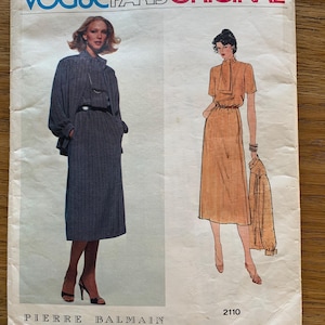 May include: A Vogue Paris Original sewing pattern envelope, number 2110, featuring Pierre Balmain designs. The cover displays two illustrations: one of a dark blue polka-dot dress and jacket, and another of a solid tan dress and matching jacket.