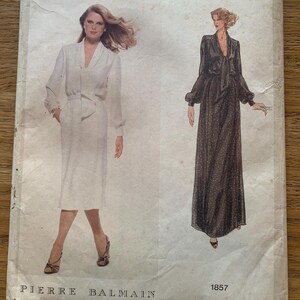 May include: Vintage Vogue Paris Original sewing pattern with two dress designs. One is a white dress with a V-neck, the other a long black dress with a bow. The pattern is labelled "Pierre Balmain" and "1857".