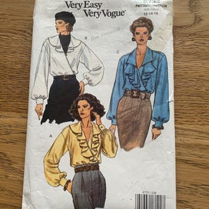 May include: A Very Easy Very Vogue sewing pattern envelope 8732 for sizes 12-14-16. The front features illustrations of three blouses with ruffled fronts and long sleeves, paired with skirts or trousers. A barcode is printed at the bottom right.
