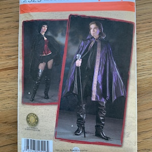 Puede incluir: Patrón de costura Simplicity con dos diseños de disfraces. Un diseño incluye una capa negra con forro morado, y el otro una capa y un corsé negros. El número de patrón es 2529.