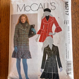 May include: A McCall's M5717 sewing pattern envelope featuring illustrations of three coat variations. The designs include a plaid coat with a ruffled hem, a solid red coat with flared sleeves, and a belted dark plaid coat with a ruffled hem.