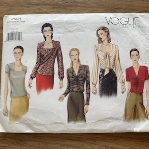 May include: A white Vogue Basic Design sewing pattern envelope labeled 2504, featuring illustrations of five different top styles labeled A through E. The tops include various necklines, sleeve lengths, and fabric patterns, displayed on figures.