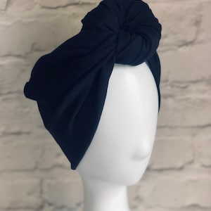 May include: A black turban headband with a knotted top. The headband is made of a soft, stretchy fabric.