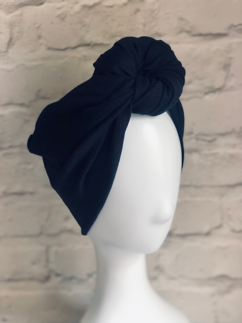 May include: A black turban headband with a knotted top. The headband is made of a soft, stretchy fabric.