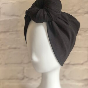 May include: A black fabric headband with a knotted top. The headband is worn on a white mannequin head.