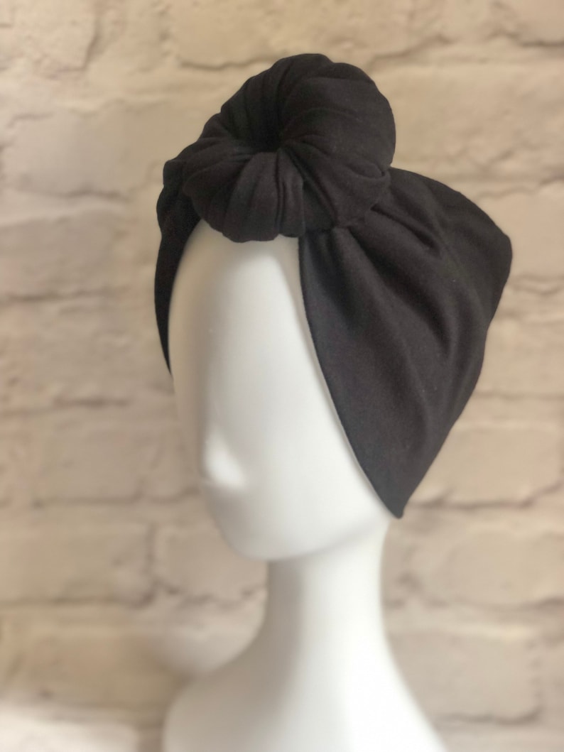 May include: A black fabric headband with a knotted top. The headband is worn on a white mannequin head.