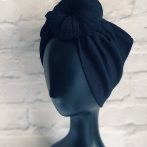 May include: A black turban with a knotted bun on top. The turban is made of a soft, stretchy fabric.