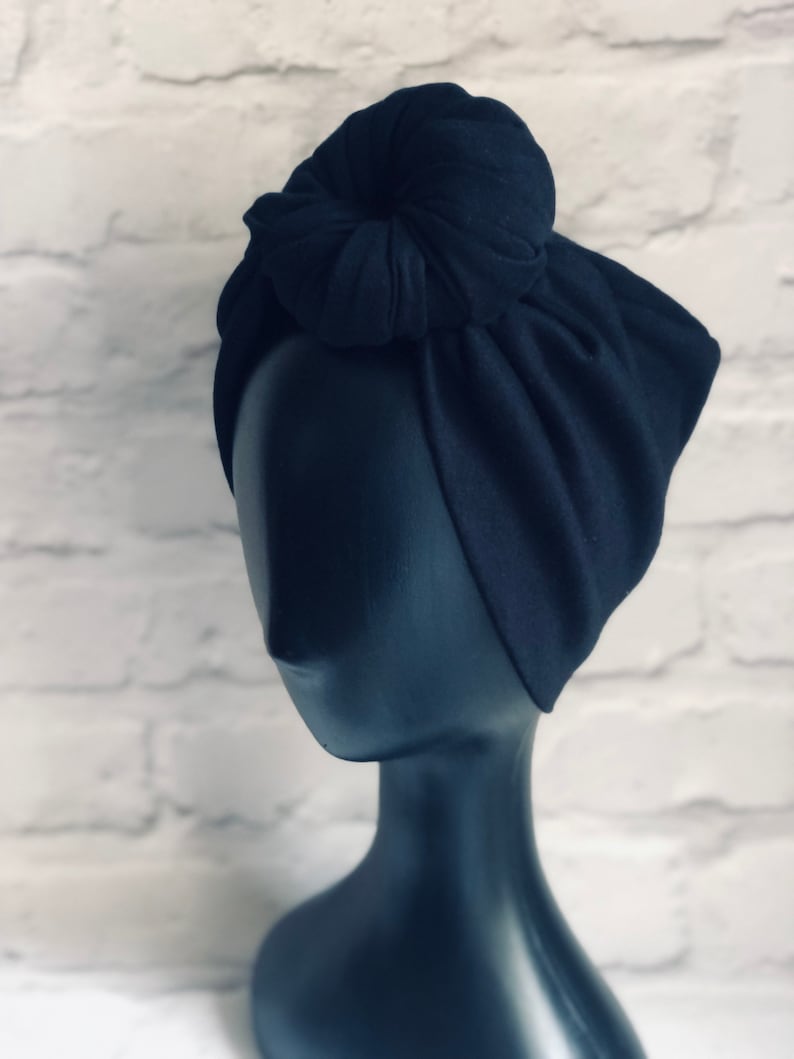 May include: A black turban with a knotted bun on top. The turban is made of a soft, stretchy fabric.