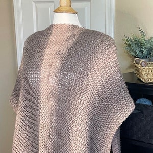 May include: A soft, knitted shawl in a gradient of brown and beige colors. The shawl is draped over a mannequin and has a loose, flowing fit.