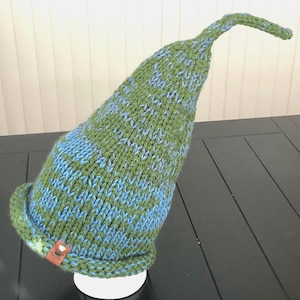 May include: A green and blue knitted hat with a long pointed top. The hat has a small tag with the word "Snug" on it.