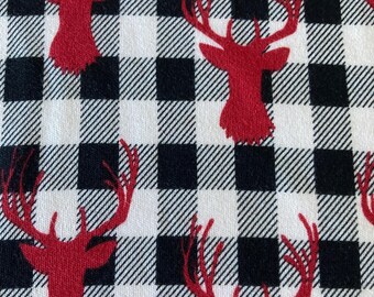 May include: A fabric with a black and white buffalo plaid pattern. Red deer silhouettes are evenly spaced across the fabric. The deer have large antlers and are facing different directions. The fabric is likely used for home decor or seasonal crafts.