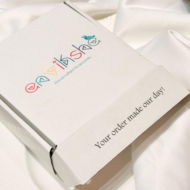 Puede incluir: Una caja de env&iacute;o de cart&oacute;n blanco con el logotipo colorido "envikshe Handcrafted Accessories" y un peque&ntilde;o icono de p&aacute;jaro. La solapa de la caja tiene impreso el texto negro "Your order made our day!" en una fuente sans-serif clara.