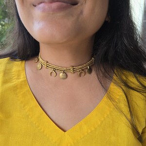 Puede incluir: Un collar tipo gargantilla de tono dorado con tres filas horizontales de peque&ntilde;as cuentas texturizadas conectadas por espaciadores rectangulares. El collar est&aacute; adornado con dijes colgantes alternos en forma de peque&ntilde;os c&iacute;rculos s&oacute;lidos y medias lunas.